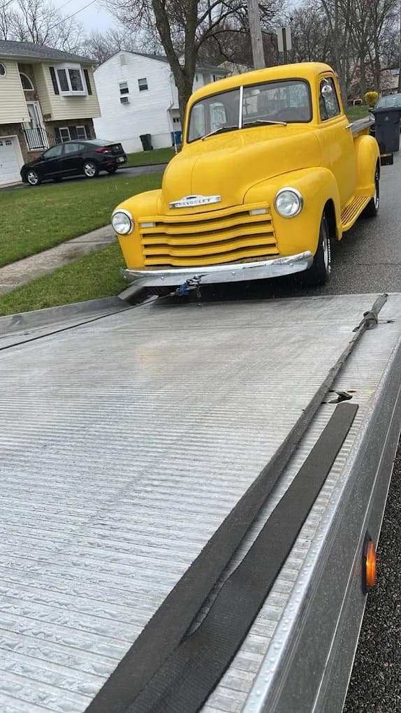 Vintage yellow Chevrolet pickup truck being loaded onto flatbed